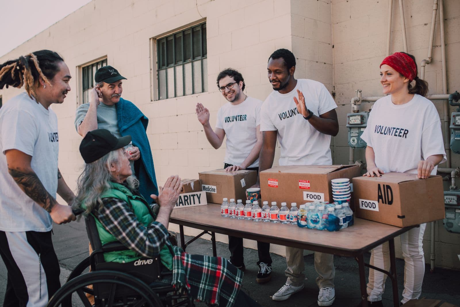Diverse group of volunteers providing food and aid to a neighbor in a wheelchair at an outdoor community event